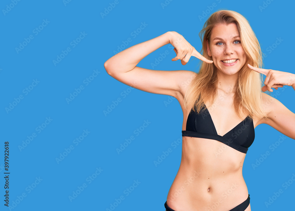 Young beautiful blonde woman wearing bikini smiling cheerful showing and pointing with fingers teeth and mouth. dental health concept. Young beautiful blonde woman wearing bikini smiling cheerful showing and pointing with fingers teeth and mouth. dental health concept.