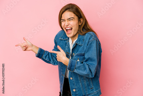 Young skinny caucasian teenager girl pointing with forefingers to a copy space, expressing excitement and desire.