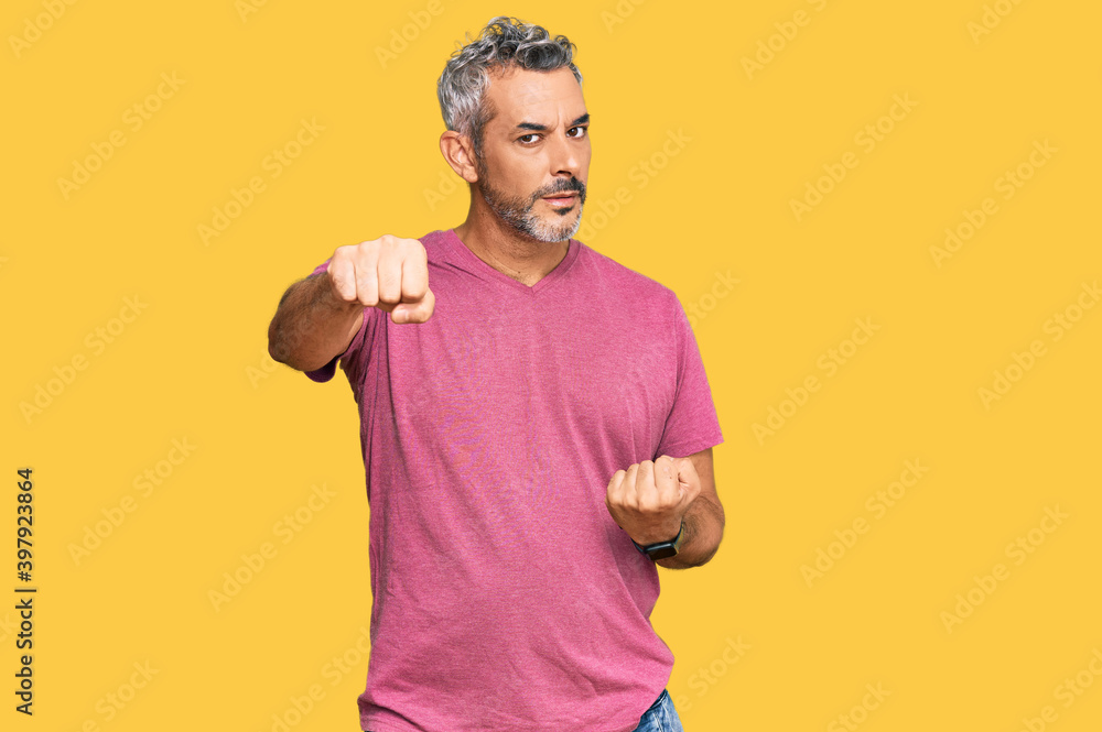 Middle age grey-haired man wearing casual clothes punching fist to fight, aggressive and angry attack, threat and violence Middle age grey-haired man wearing casual clothes punching fist to fight, aggressive and angry attack, threat and violence