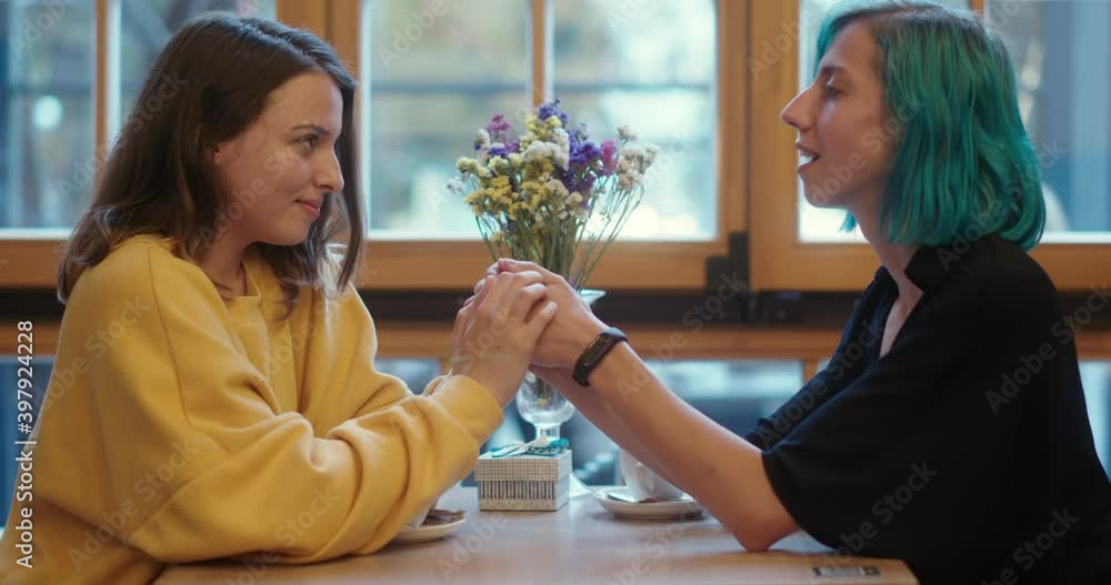 Romantic young gay women in a same sex relationship enjoying a cup of coffee at a restaurant seated at table holding hands and smiling at each other Romantic young gay women in a same sex relationship enjoying a cup of coffee at a restaurant seated at table holding hands and smiling at each other