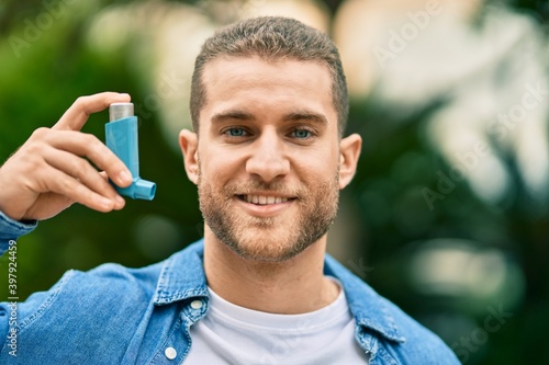 Young caucasian asthmatic man smiling happy holding inhaler at the park.