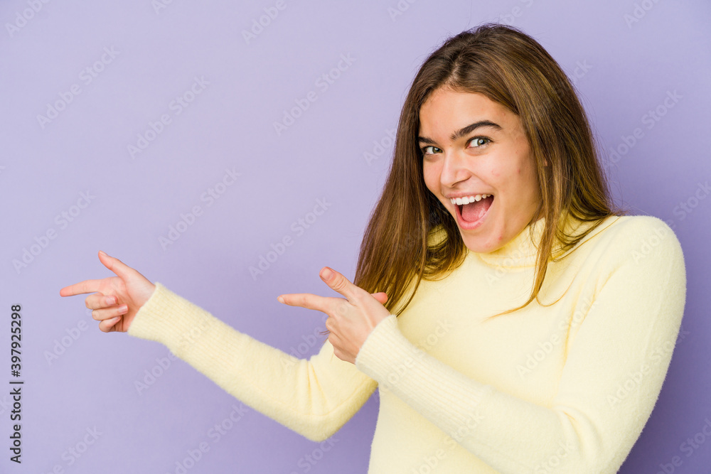 Young skinny caucasian girl teenager on purple background excited pointing with forefingers away. Young skinny caucasian girl teenager on purple background excited pointing with forefingers away.