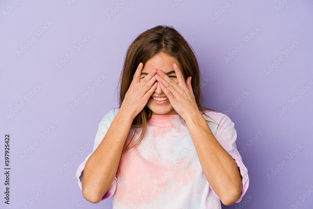 Young skinny caucasian girl teenager on purple background blink at the camera through fingers, embarrassed covering face. Young skinny caucasian girl teenager on purple background blink at the camera through fingers, embarrassed covering face.