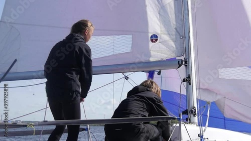 Slowmotion shot. A young guy pulls ropes on a sailing yacht during a regatta on the river, the girls help