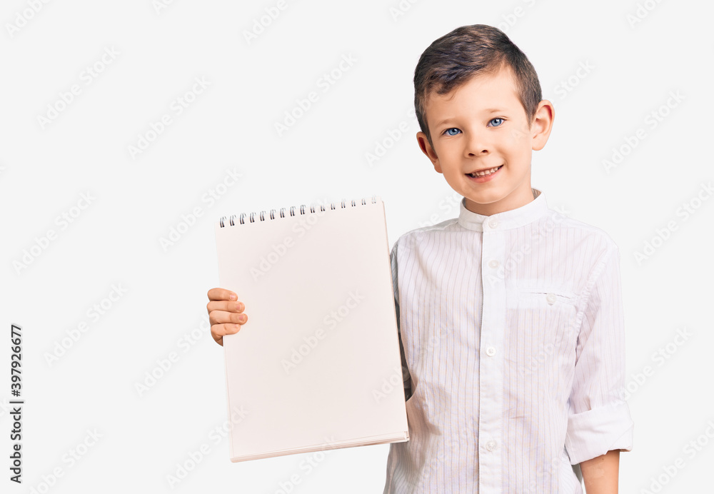 Cute blond kid holding notebook looking positive and happy standing and smiling with a confident smile showing teeth Cute blond kid holding notebook looking positive and happy standing and smiling with a confident smile showing teeth