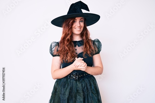 Young beautiful woman wearing witch halloween costume with hands together and crossed fingers smiling relaxed and cheerful. success and optimistic