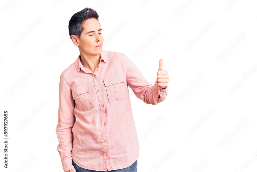 Young woman with short hair wearing casual clothes looking proud, smiling doing thumbs up gesture to the side Young woman with short hair wearing casual clothes looking proud, smiling doing thumbs up gesture to the side