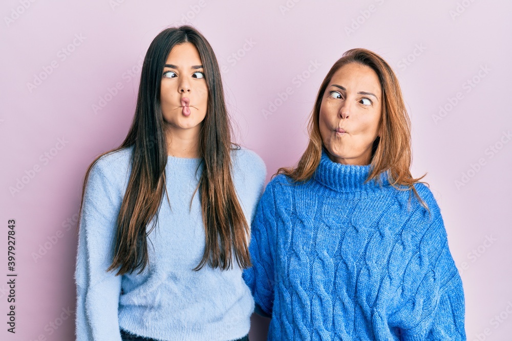 Hispanic family of mother and daughter wearing wool winter sweater making fish face with lips, crazy and comical gesture. funny expression. Hispanic family of mother and daughter wearing wool winter sweater making fish face with lips, crazy and comical gesture. funny expression.