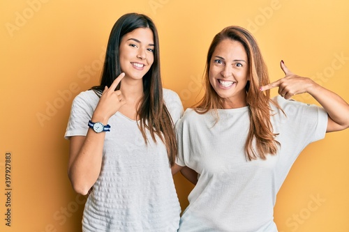 Hispanic family of mother and daughter wearing casual white tshirt smiling cheerful showing and pointing with fingers teeth and mouth. dental health concept.
