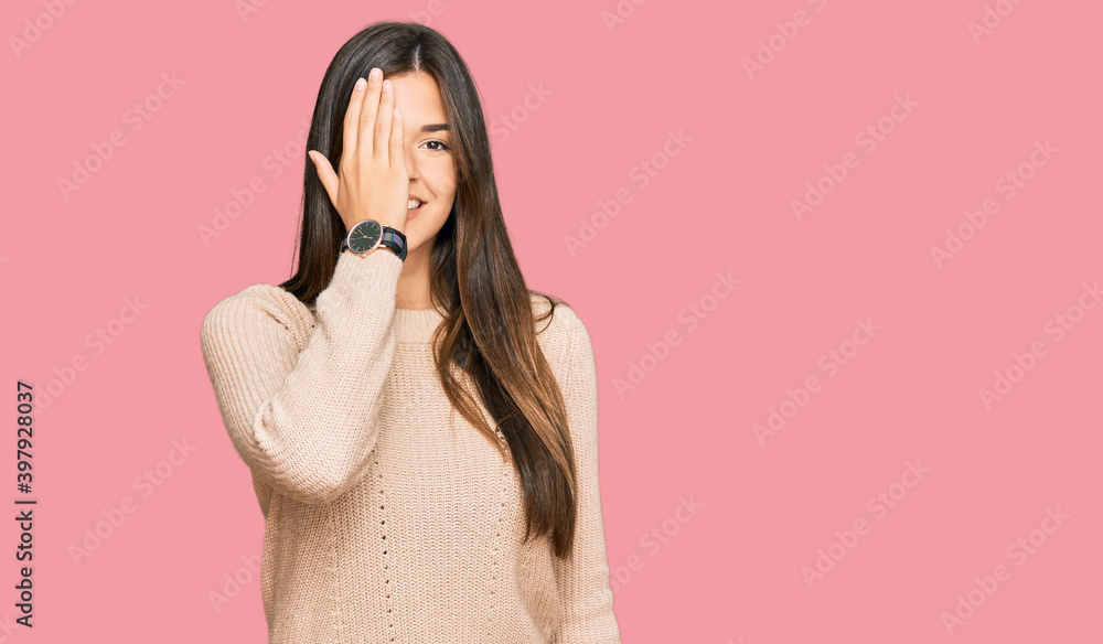 Young brunette woman wearing casual winter sweater covering one eye with hand, confident smile on face and surprise emotion. Young brunette woman wearing casual winter sweater covering one eye with hand, confident smile on face and surprise emotion.