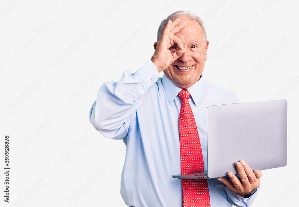 Senior handsome grey-haired man wearing tie using laptop smiling happy doing ok sign with hand on eye looking through fingers Senior handsome grey-haired man wearing tie using laptop smiling happy doing ok sign with hand on eye looking through fingers