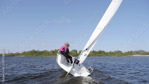 A young man and two girls cut through the waves of the lake on a white sailing boat in slow motion.