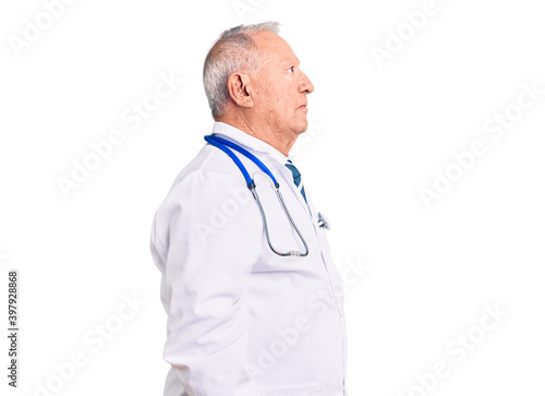 Senior handsome grey-haired man wearing doctor coat and stethoscope looking to side, relax profile pose with natural face and confident smile.