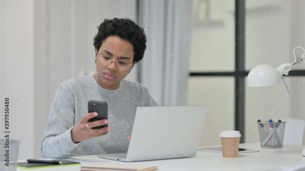 African Woman with Laptop using Smartphone at Work African Woman with Laptop using Smartphone at Work