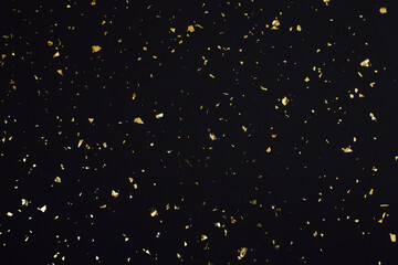 Gold confetti on black background. Festive holiday backdrop. Birthday congratulations Christmas New Year. Flat lay, top view, copy space.