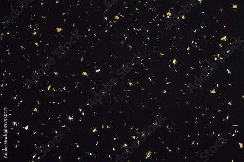 Gold confetti on black background. Festive holiday backdrop. Birthday congratulations Christmas New Year. Flat lay, top view, copy space.
