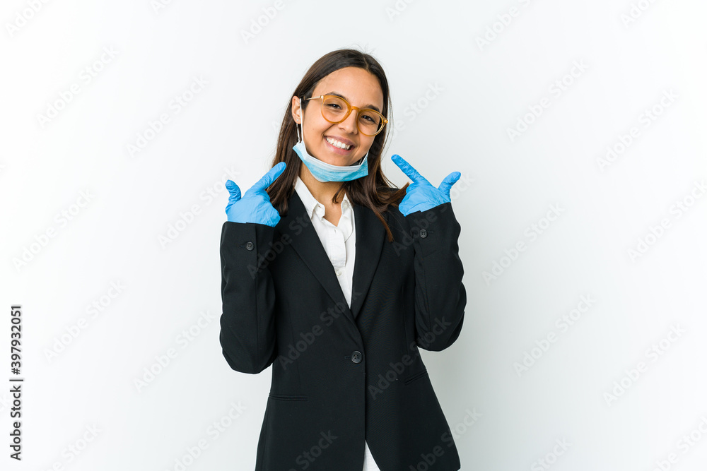 Young business latin woman wearing a mask to protect from covid isolated on white background smiles, pointing fingers at mouth. Young business latin woman wearing a mask to protect from covid isolated on white background smiles, pointing fingers at mouth.