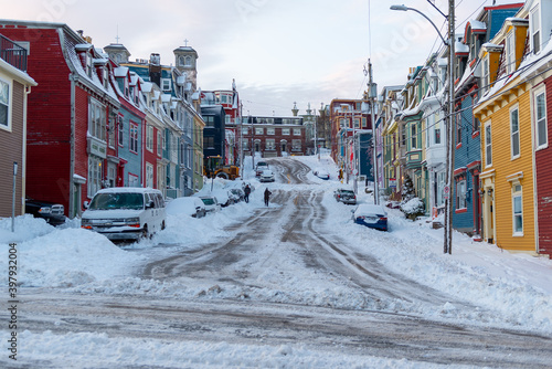 Fototapeta Naklejka Na Ścianę i Meble -  A narrow street in downtown St. John's, covered in fresh white snow after a snowstorm. The houses on both sides of the paved street are colourful small wooden rows of joined residential buildings.  