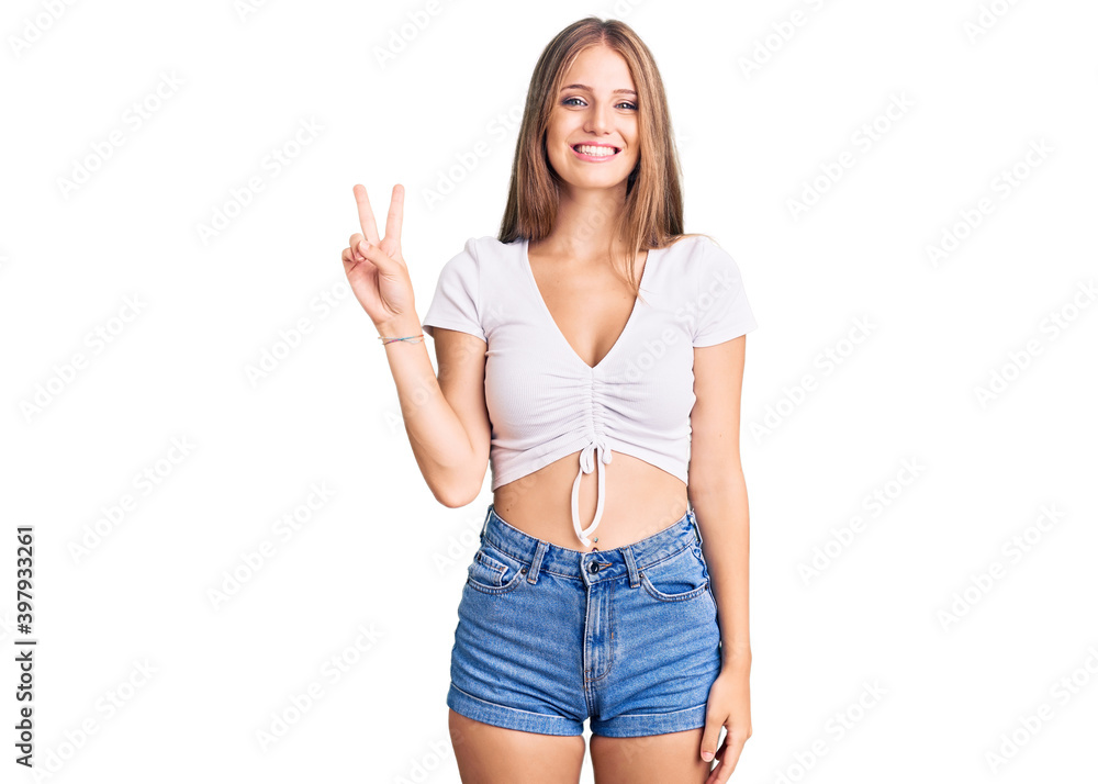 Young beautiful blonde woman wearing casual white tshirt smiling looking to the camera showing fingers doing victory sign. number two. Young beautiful blonde woman wearing casual white tshirt smiling looking to the camera showing fingers doing victory sign. number two.