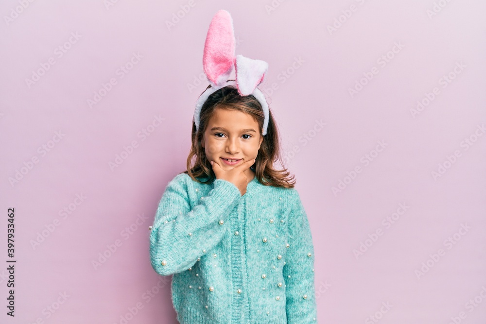 Little beautiful girl wearing cute easter bunny ears looking confident at the camera smiling with crossed arms and hand raised on chin. thinking positive. Little beautiful girl wearing cute easter bunny ears looking confident at the camera smiling with crossed arms and hand raised on chin. thinking positive.