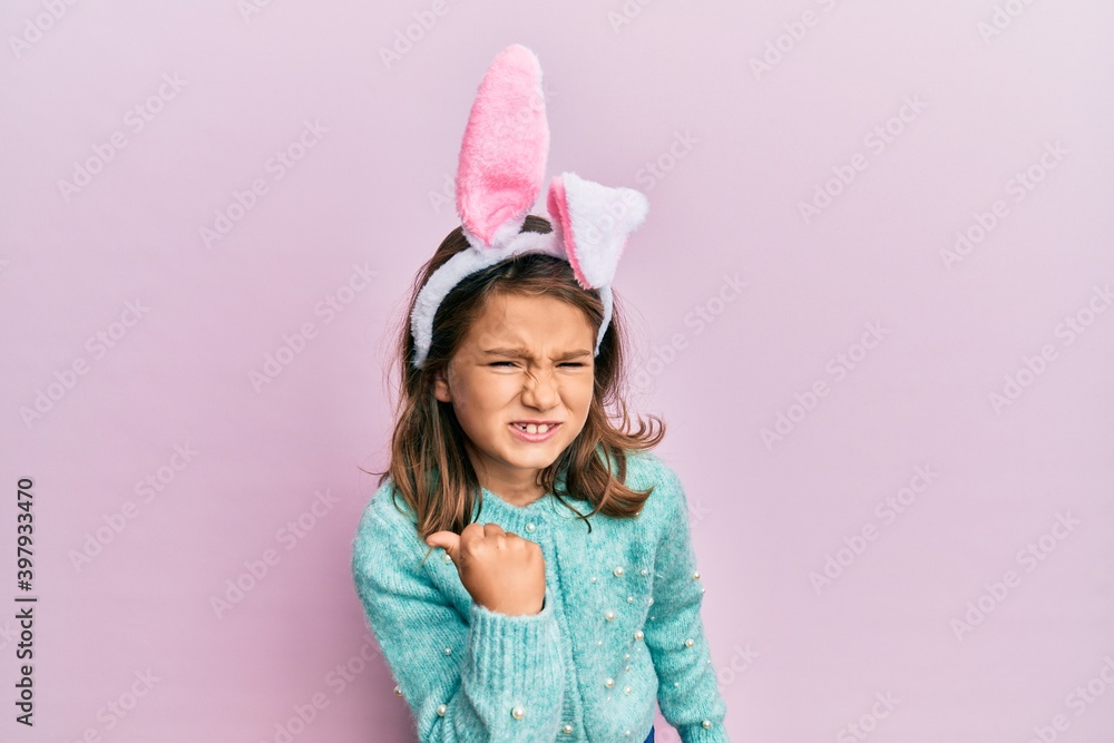 Little beautiful girl wearing cute easter bunny ears angry and mad raising fist frustrated and furious while shouting with anger. rage and aggressive concept. Little beautiful girl wearing cute easter bunny ears angry and mad raising fist frustrated and furious while shouting with anger. rage and aggressive concept.