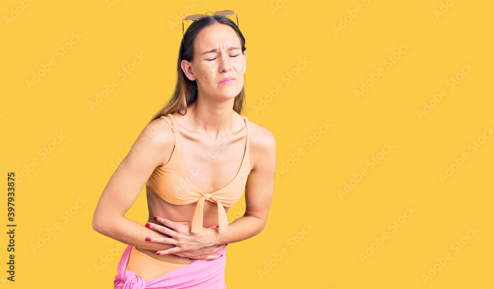 Obraz premium Beautiful brunette young woman wearing bikini and sunglasses with hand on stomach because indigestion, painful illness feeling unwell. ache concept.