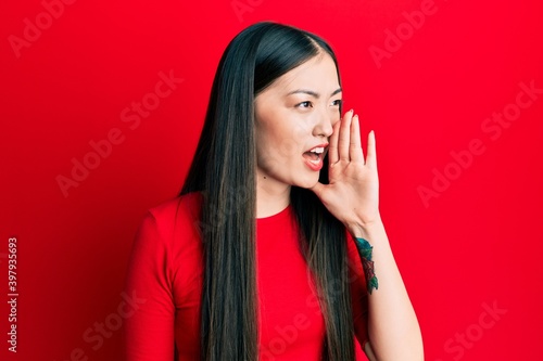 Young chinese woman wearing casual clothes shouting and screaming loud to side with hand on mouth. communication concept.