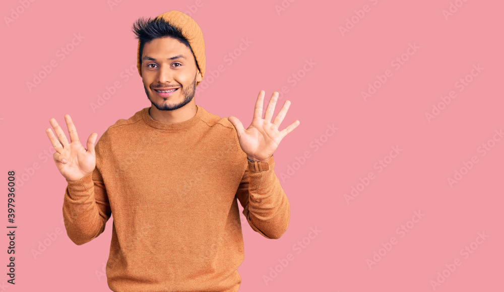 Handsome latin american young man wearing winter sweater and wool hat showing and pointing up with fingers number nine while smiling confident and happy. Handsome latin american young man wearing winter sweater and wool hat showing and pointing up with fingers number nine while smiling confident and happy.
