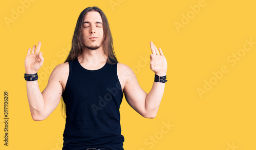 Photography Young adult man with long hair wearing rocker style with black clothes and contact lenses relax and smiling with eyes closed doing meditation gesture with fingers