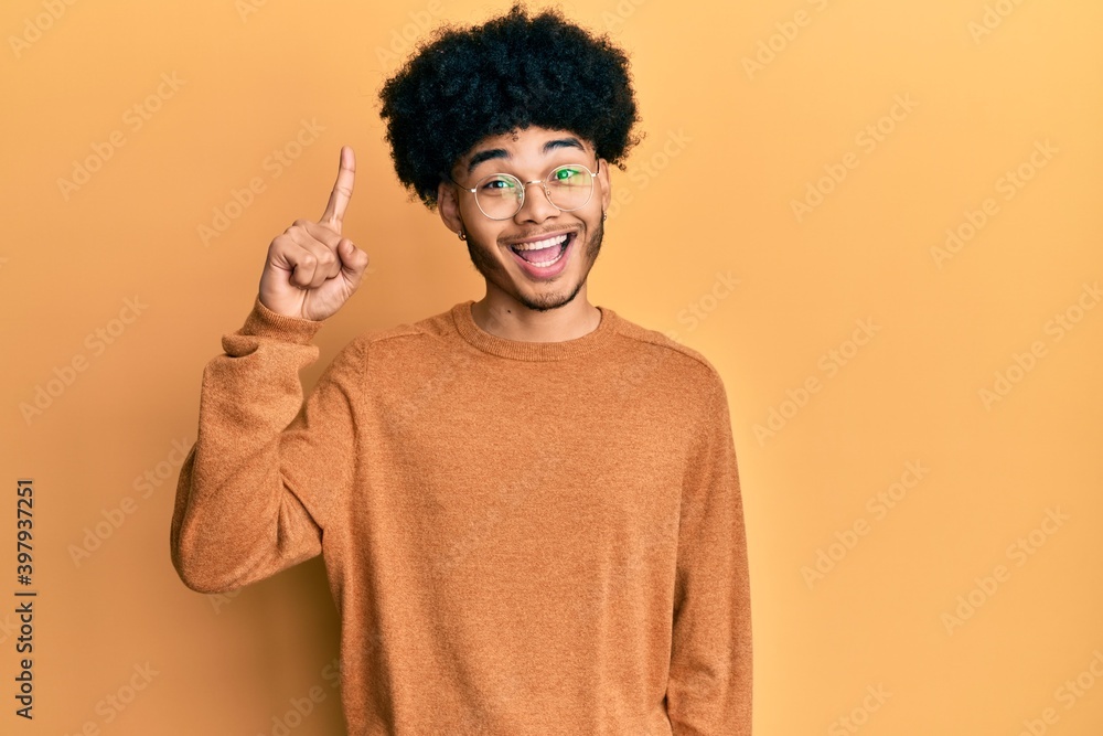 Young african american man with afro hair wearing casual winter sweater pointing finger up with successful idea. exited and happy. number one. Young african american man with afro hair wearing casual winter sweater pointing finger up with successful idea. exited and happy. number one.