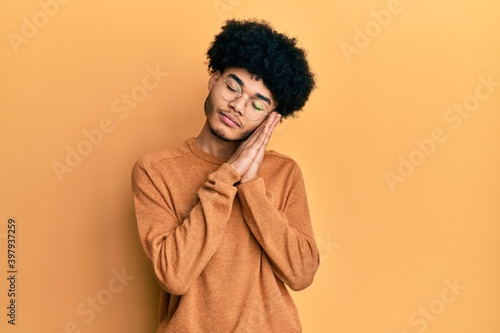 Young african american man with afro hair wearing casual winter sweater sleeping tired dreaming and posing with hands together while smiling with closed eyes.
