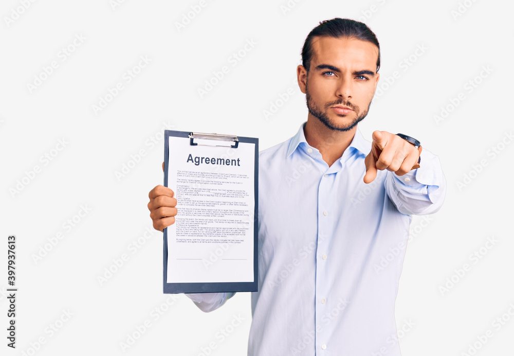 Young handsome man holding clipboard with agreement document pointing with finger to the camera and to you, confident gesture looking serious Young handsome man holding clipboard with agreement document pointing with finger to the camera and to you, confident gesture looking serious