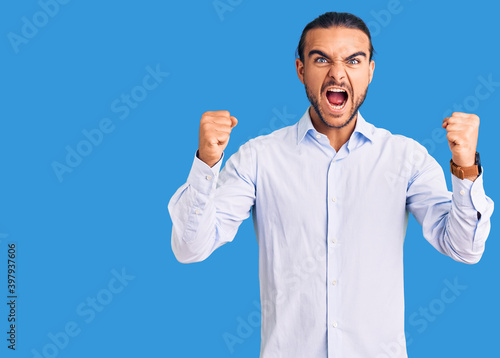 Young handsome man wearing business clothes angry and mad raising fists frustrated and furious while shouting with anger. rage and aggressive concept.