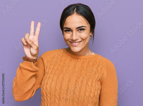 Young brunette woman wearing casual winter sweater showing and pointing up with fingers number two while smiling confident and happy.