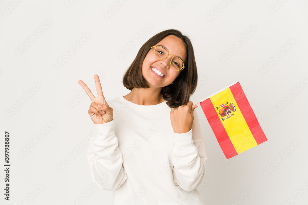 Young hispanic mixed race woman holding a spanish flag joyful and carefree showing a peace symbol with fingers. Young hispanic mixed race woman holding a spanish flag joyful and carefree showing a peace symbol with fingers.