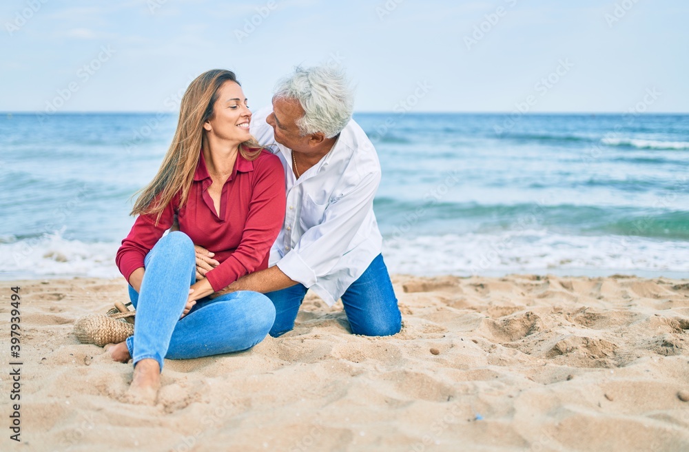 Middle age hispanic couple smiling happy and hugging sitting at the beach Middle age hispanic couple smiling happy and hugging sitting at the beach