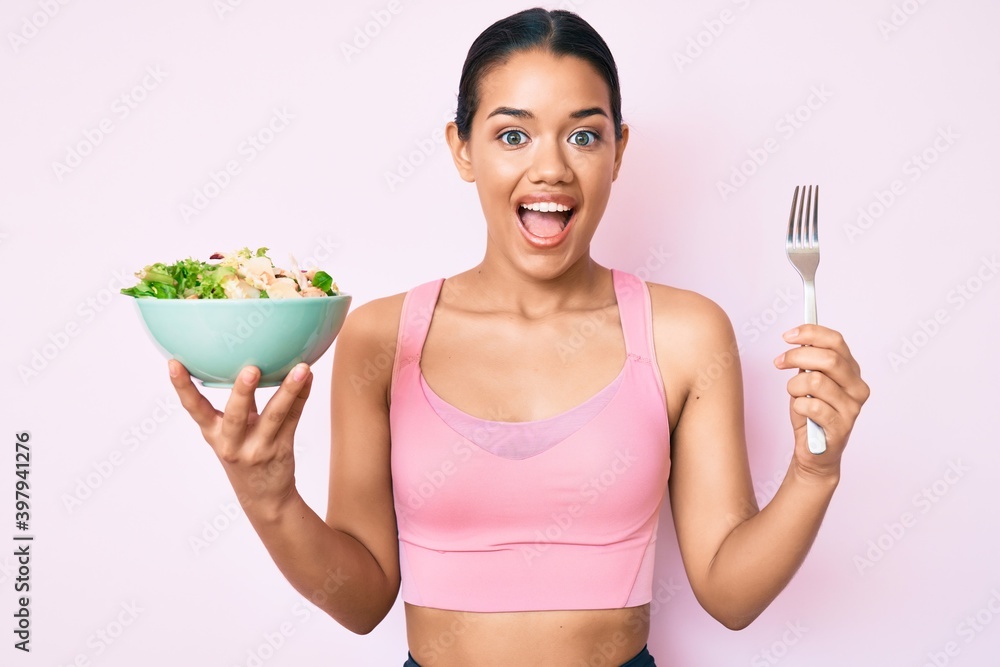 Young beautiful latin girl wearing sportswear holding salad celebrating crazy and amazed for success with open eyes screaming excited. Young beautiful latin girl wearing sportswear holding salad celebrating crazy and amazed for success with open eyes screaming excited.