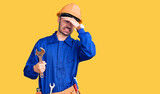 Young hispanic man wearing electrician uniform holding wrench stressed and frustrated with hand on head, surprised and angry face
