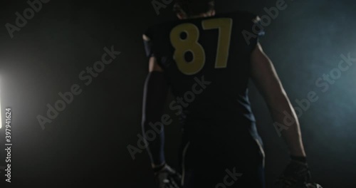 Tracking shot of of American football sportsman player walking on abstract black smoke background