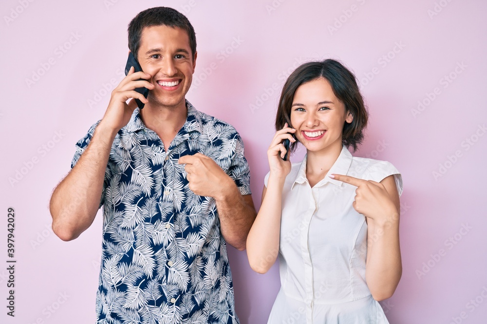 Beautiful couple having conversation talking on the smartphone pointing finger to one self smiling happy and proud Beautiful couple having conversation talking on the smartphone pointing finger to one self smiling happy and proud