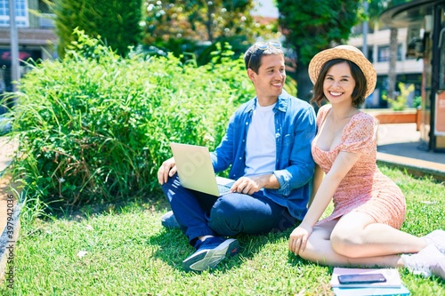 Beautiful couple smiling happy sitting on the grass using laptop at park
