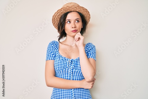 Young beautiful girl wearing summer hat thinking concentrated about doubt with finger on chin and looking up wondering