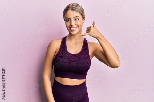 Fototapeta Naklejka Na Ścianę i Meble -  Beautiful blonde woman wearing sportswear over pink background smiling doing phone gesture with hand and fingers like talking on the telephone. communicating concepts.
