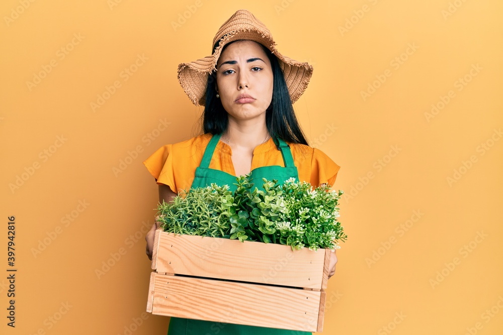 Beautiful young woman wearing gardener apron holding wooden plant pot depressed and worry for distress, crying angry and afraid. sad expression.
