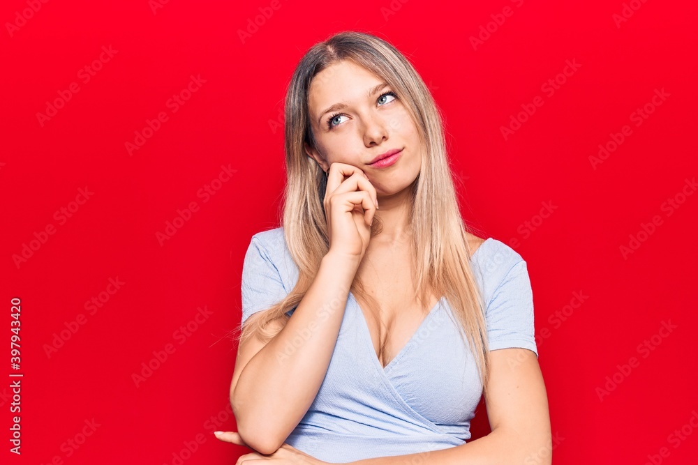 Young blonde woman wearing casual clothes thinking concentrated about doubt with finger on chin and looking up wondering Young blonde woman wearing casual clothes thinking concentrated about doubt with finger on chin and looking up wondering