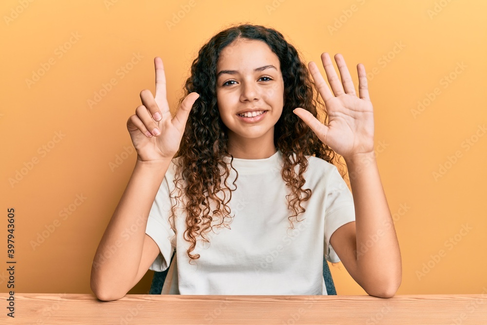 Teenager hispanic girl wearing casual clothes sitting on the table showing and pointing up with fingers number seven while smiling confident and happy. Teenager hispanic girl wearing casual clothes sitting on the table showing and pointing up with fingers number seven while smiling confident and happy.