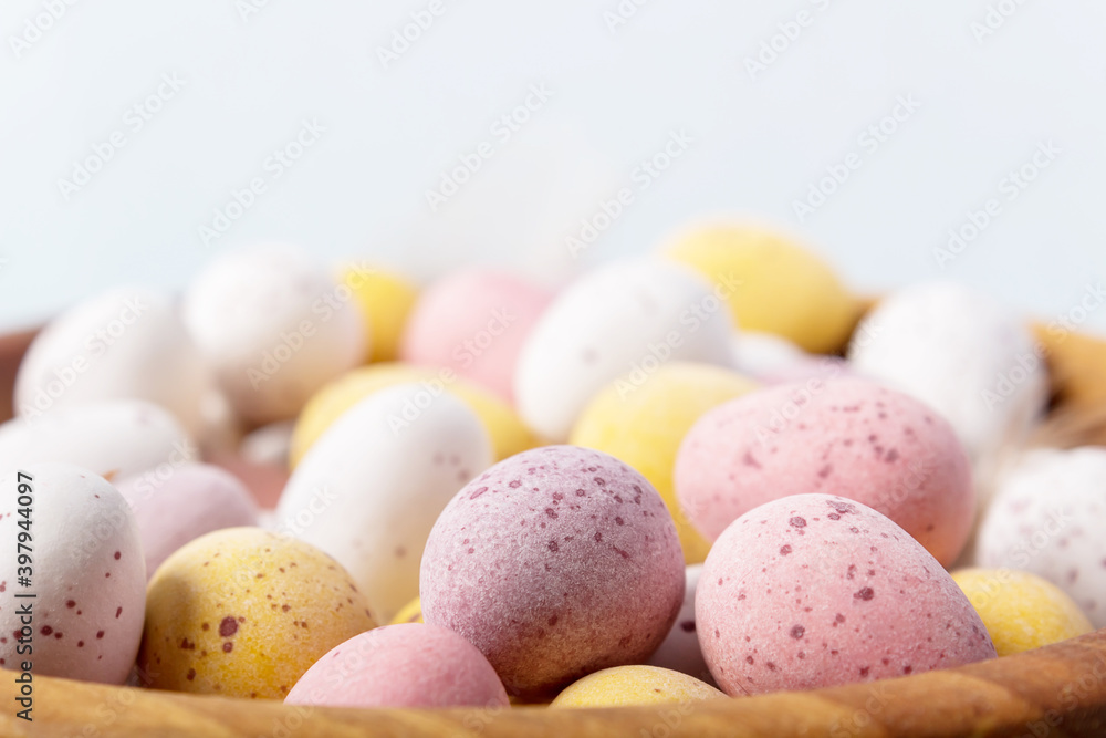 Close up Easter eggs in wooden bowl on blue background. Selective focus. Close-up. White yellow pink eggs for Easter treat. Close up Easter eggs in wooden bowl on blue background. Selective focus. Close-up. White yellow pink eggs for Easter treat.