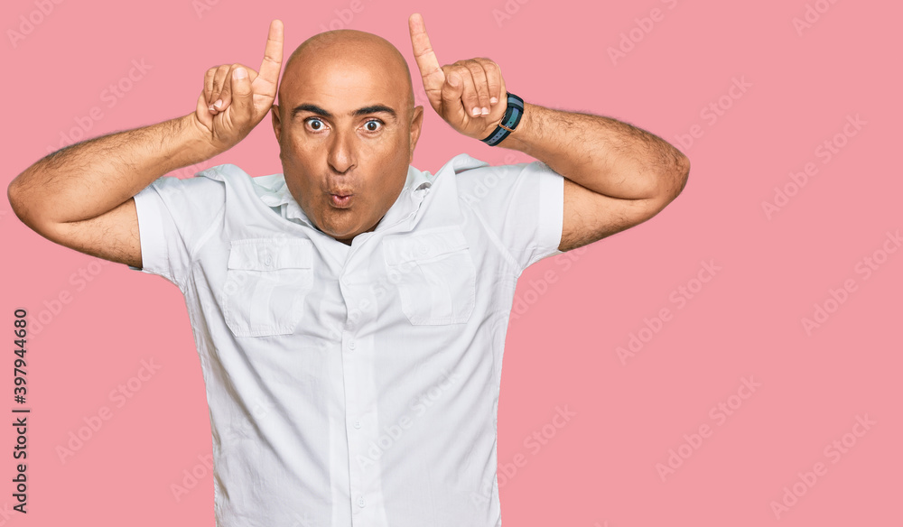 Mature middle east man with mustache wearing casual white shirt doing funny gesture with finger over head as bull horns Mature middle east man with mustache wearing casual white shirt doing funny gesture with finger over head as bull horns