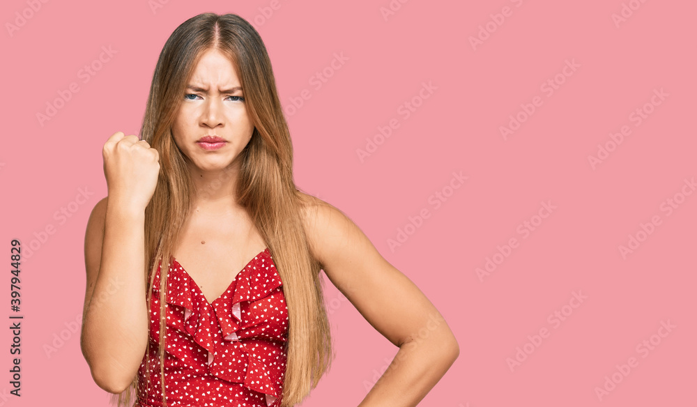 Beautiful blonde woman wearing summer dress angry and mad raising fist frustrated and furious while shouting with anger. rage and aggressive concept. Beautiful blonde woman wearing summer dress angry and mad raising fist frustrated and furious while shouting with anger. rage and aggressive concept.