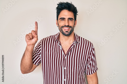Handsome hispanic man with beard wearing casual clothes pointing finger up with successful idea. exited and happy. number one.